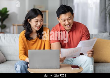 Glückliche asiatische Ehegatten zahlen Rechnungen online, mit Laptop Stockfoto