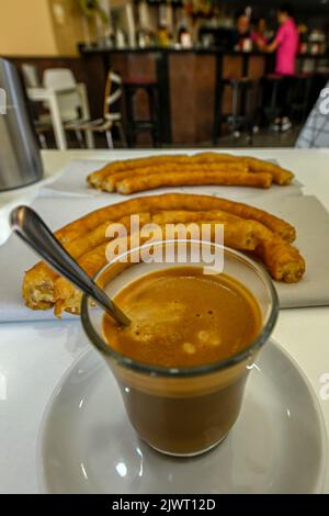 Ein Glas Kaffee mit Milch und Churros in einer Cafeteria. Stockfoto