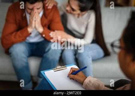 Behandlung von Depressionen. Unglückliche kaukasische Frau beruhigt den weinenden Mann nach Rücksprache mit dem Psychologen Stockfoto