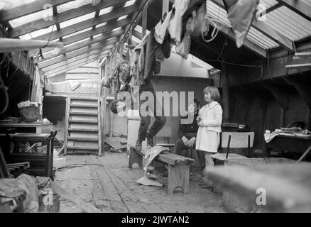 London, England, um 1967. Eine Gruppe von Kindern des Piratenclubs an Bord von ‘Rosedale’, einem ausgedienten Lastkahn, der als Clubhaus diente. Zwei Jungen schwingen von einem Dachbalken, während ein anderer Junge und ein anderes Mädchen sich ansehen. Gebrauchte Nägel und andere Abfälle wurden auf dem Deck des Lastkahns, die von den Restaurierungsarbeiten übrig geblieben sind, weggeworfen. Der Pirate Club, ein Kinderbootclub, wurde 1966 in Gilbey’s Wharf am Regent’s Canal in der Nähe von Camden, London, gegründet. Für die Kinder wurden eine Reihe kleiner Boote und Kanus gespendet. Stockfoto