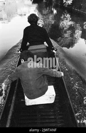 London, England, um 1967. Drei Jungen des Piratenclubs an Bord eines kleinen Bootes auf dem Regent’s Canal. Ein Junge zieht seine Finger durch das Wasser. Der Pirate Club, ein Kinderbootclub, wurde 1966 in Gilbey’s Wharf am Regent’s Canal in der Nähe von Camden, London, gegründet. Ihr Klubhaus war ein alter Lastkahn und eine Reihe kleiner Boote und Kanus wurden für die Kinder gespendet. Stockfoto