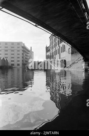 London, England, um 1967. Ein Blick unter einer eisernen Fußgängerbrücke über einen Abschnitt des Regent’s Canal zwischen Oval Road und Camden High Street. Zwei Jungen, die Mitglieder des Pirate Club sind, segeln in einem kleinen Schlauchboot. Gilbey House und die Oval Road Bridge sind in der Ferne zu sehen. Der Pirate Club, ein Kinderbootclub, wurde 1966 in Gilbey's Wharf am Regents Canal in der Nähe von Camden, London, gegründet. Ihr Klubhaus war ein alter Lastkahn und eine Reihe kleiner Boote und Kanus wurden für die Kinder gespendet. Stockfoto