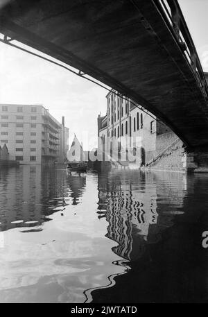 London, England, um 1967. Ein Blick unter einer eisernen Fußgängerbrücke über einen Abschnitt des Regent’s Canal zwischen Oval Road und Camden High Street. Zwei Jungen, die Mitglieder des Pirate Club sind, segeln in einem kleinen Schlauchboot. Gilbey House und die Oval Road Bridge sind in der Ferne zu sehen. Der Pirate Club, ein Kinderbootclub, wurde 1966 in Gilbey's Wharf am Regents Canal in der Nähe von Camden, London, gegründet. Ihr Klubhaus war ein alter Lastkahn und eine Reihe kleiner Boote und Kanus wurden für die Kinder gespendet. Stockfoto