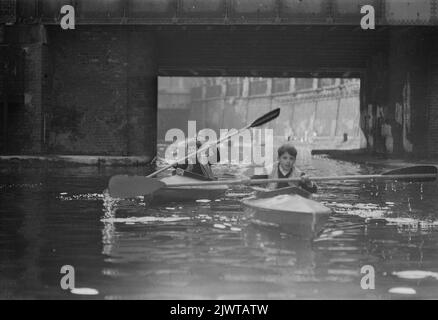 London, England, um 1967. Zwei Jungen, die Mitglieder des Pirate Club sind, paddeln Kanus auf dem Regents Canal in Camden, nachdem sie gerade die Oval Road Bridge passiert haben. Der Pirate Club, ein Kinderbootclub, wurde 1966 in Gilbey's Wharf am Regents Canal in der Nähe von Camden, London, gegründet. Ihr Klubhaus war ein alter Lastkahn und eine Reihe kleiner Boote und Kanus wurden für die Kinder gespendet. Stockfoto