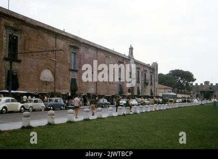 Pisa, Toskana, Italien, 1963. Eine Reihe von Touristenbuden vor dem Museum von Sinopie; auf der Piazza dei Miracoli. Entlang der Straße werden verschiedene Autos geparkt, darunter ein Volkswagen Beetle, ein Fiat 1100 Familiare und ein Fiat 600. Touristen fotografieren den schiefen Turm von Pisa, der sich gegenüber und außer Schuss befindet. Stockfoto