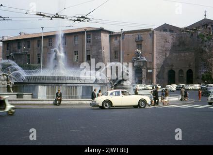 Rom, 1963. Blick auf den Brunnen der Naiads, der sich im Zentrum der Piazza della Repubblica auf dem Viminal-Hügel befindet. Der Brunnen wurde 1888 vom Architekten Alessandro Guerrieri geschaffen. Bronzeskulpturen von Najaden und einem anderen Gott des Glaucus wurden von Mario Rutelli geschaffen und 1901 und 1912 hinzugefügt. Ein Jaguar Mk.II wartet, während Fußgänger die Straße vor ihm überqueren. Hinter dem Brunnen befindet sich der Eingang zur Basilika St. Maria der Engel und der Märtyrer. Stockfoto