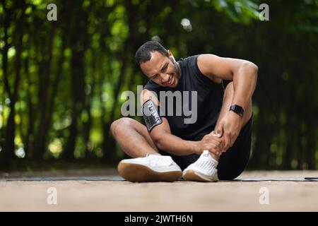 afroamerikanischer Athlet, der Schmerzen hat und seinen Knöchel berührt Stockfoto