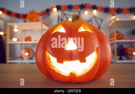 Nahaufnahme der gruseligen orangefarbenen Halloween Jack-o-Laterne, die auf dem Tisch im dekorierten Raum platziert ist Stockfoto