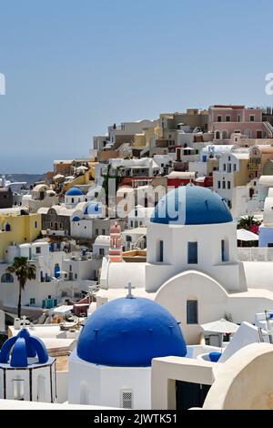 Oia, Santorini, Griechenland - Juni 2022: Traditionelle weißgetünchte Gebäude mit blauen Kuppeln mit Blick auf das Meer in Oia Stockfoto