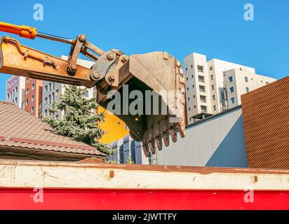 Aushubarbeiten. Der Eimer des Traktors lädt den Boden mit einer Schaufel in die Rückseite eines Muldenkipper auf der Baustelle. Stockfoto