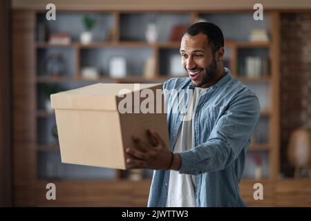 Lieferkonzept. Fröhlicher Junger Schwarzer Mann, Der Zu Hause Große Karton-Schachtel Hält Stockfoto