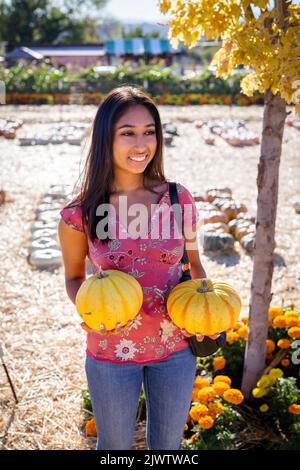 Herbstfest Porträt einer jungen Asiatin, die zwei Kürbisse auf einer Farm hält Stockfoto