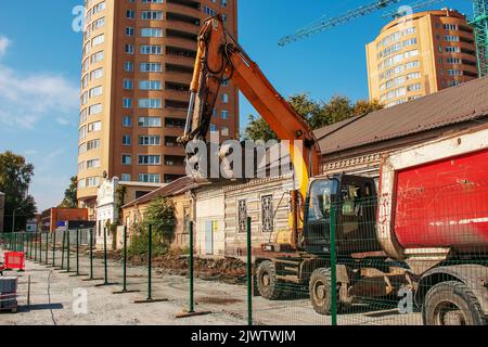 Aushubarbeiten. Der Eimer des Traktors lädt den Boden mit einer Schaufel in die Rückseite eines Muldenkipper auf der Baustelle. Stockfoto