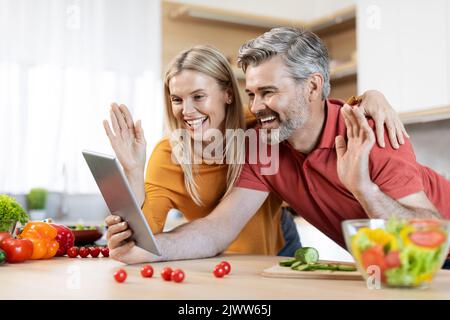 Glücklicher Mann und Frau beim Kochen mit einem digitalen Tablet Stockfoto