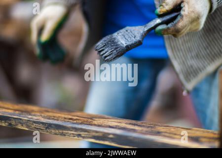 Ein Mann trägt mit einem Pinsel Farbe auf eine Holzfläche auf. Lackarbeiten Stockfoto