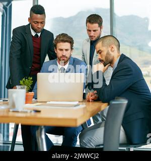 Sicherstellen, dass ihr Spielplan wasserdicht ist. Ein Team von Kollegen, das in einem modernen Büro ein Meeting um einen Laptop herum abgeht. Stockfoto