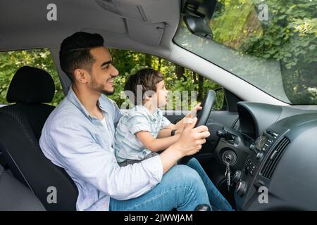 Glücklich lächelnd muslim jungen Mann lehrt kleines Kind, wie man fährt, Profil. Vater und Sohn bekamen Fahrunterricht, neues Auto Stockfoto