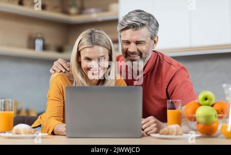 Glückliche Ehegatten mit Laptop beim Essen in der Küche Stockfoto