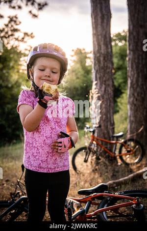 Ein kleines Mädchen, das vor dem Fahrrad steht, isst einen Apfel Stockfoto