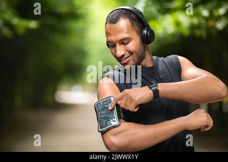 Positive afroamerikanische Sportler berühren Smartphone in Armband Stockfoto