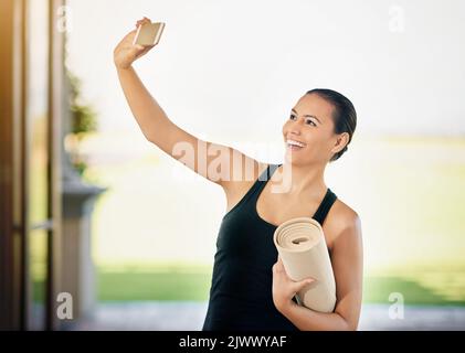 Yoga Selfie. Eine junge Frau, die ein Selfie macht, während sie ihre Yogamatte trägt. Stockfoto