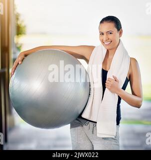 Lächelnd, weil ich fit bin. Beschnittenes Porträt einer jungen Frau, die ihren Übungsball trägt. Stockfoto