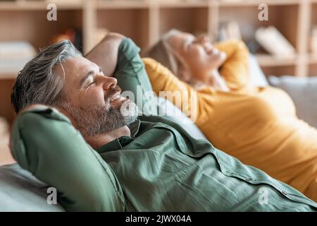 Lächelndes Paar Mittleren Alters, Das Sich Auf Einem Bequemen Sofa Zu Hause Entspannt Stockfoto