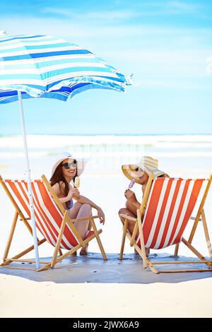 Strandliegen. Porträt zweier schöner junger Frauen, die am Strand ein Eis essen. Stockfoto