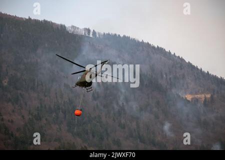 Örtlich begrenztes Wildfeuer, bei dem der Hubschrauber Wasser abtropft, indem er einen Wassereimer verwendet, der an einer langen Linie unter dem Hubschrauber befestigt ist Stockfoto