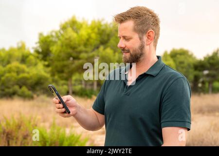 Junger kaukasischer Mann lächelt glücklich mit dem Smartphone im Park. Stockfoto