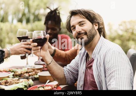Zeit mit Freunden verbringen. Gutaussehende bärtige vierzig Mann rösten mit Rotwein und lächeln, während er mit seinen Freunden im Bauernhaus Restaurant c Stockfoto