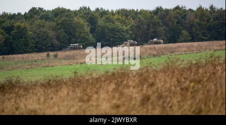 Drei Foxhound-Lichtschutzpatrouillenfahrzeuge der britischen Armee (LPPV Force Protection Ocelot), die bei einer militärischen Übung hinter Waldflächen Schutz nehmen Stockfoto