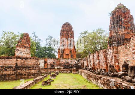 Verfallene rote Ziegelstangen und Wände mit kopflosen Buddha-Statuen in den Ruinen von Wat Maha That, dem heiligen königlichen Tempel in Ayutthaya, Thailand Stockfoto