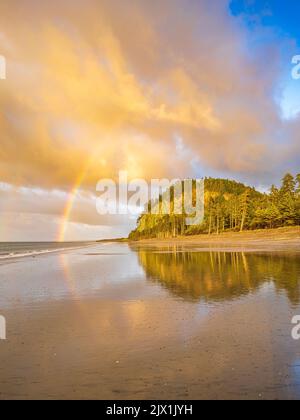 Ein spät-nachmittag Regenbogen über zwei Hügel auf dem nassen Sand bei Agate Beach in Naikoon Provincial Park, Haida Gwaii, British Columbia widerspiegelt Stockfoto