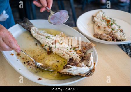 Serviert in einem Restaurant mit frischem gegrilltem Knoblauch und Olivenöl auf alten Kohleparrillas, Meerbarsch-Fisch im kleinen Fischerdorf Getaria, Baskisch Stockfoto