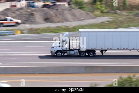 An einem sonnigen Tag ist auf einer mehrspurigen Autobahn ein leerer, weißer Auflieger und Anhänger zu sehen. Stockfoto