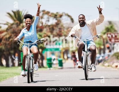 Afrikanisches Paar mit dem Fahrrad im Urlaub, Friedenshandzeichen auf dem Fahrrad für nachhaltigen Lebensstil in der Stadt und glücklich im Urlaub im Sommer für Reisen Stockfoto