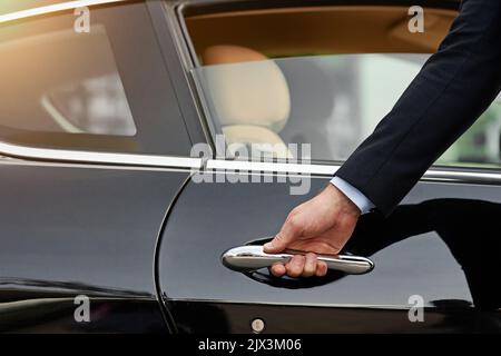 Erlauben Sie mir... ein nicht erkennbarer männlicher Chauffeur, der eine Autotür öffnet. Stockfoto