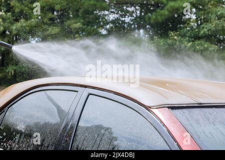 Ein Mann, der Auto mit Waschwagen unter Hochdruck-Wasserstrahl putzt Stockfoto