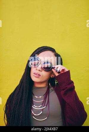 Eine junge Frau trägt eine Sonnenbrille vor grünem Hintergrund. Stockfoto