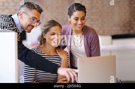 Können Sie daran Änderungen vornehmen? Ein reifer Mann hilft einer Arbeitskollegin auf ihrem Laptop im Büro. Stockfoto