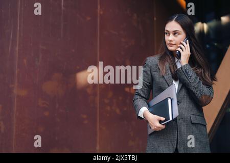 Porträt eines jungen Büroassistenten, der den Plan am Telefon diskutiert, während er während der Kaffeepause in ein Café ging. Speicherplatz kopieren. Internetkommunikation Stockfoto