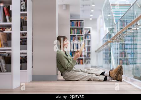 Nachdenkliche Frau mittleren Alters mit Buch, die Freizeit in der Bibliothek verbringt und gerne liest Stockfoto