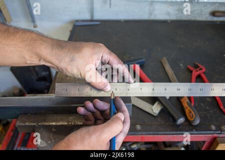 Bild der schmutzigen Hände eines Schmieds, der mit einem Lineal und einem Bleistift ein mechanisches Stück Eisen misst, das geschnitten werden soll. Machen Sie es selbst arbeiten in den Werken Stockfoto