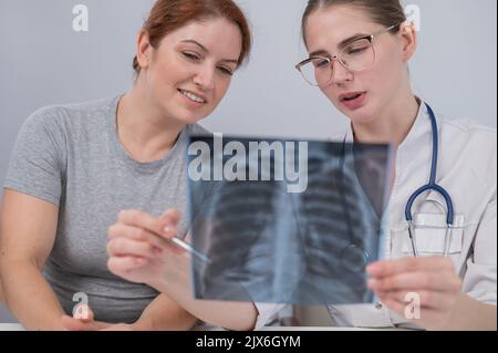 Der Arzt konsultiert eine kaukasische Frau und kommentiert die Röntgenaufnahme der Lunge. Stockfoto