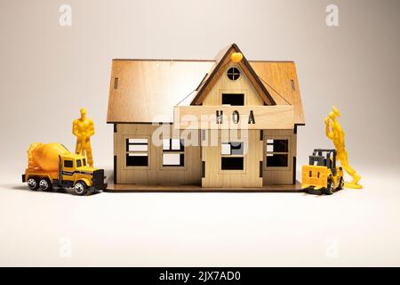 Das Wort HOA steht auf der Holzoberfläche. Arbeiter arbeiten an Holz-Miniaturhaus im Hintergrund. Business und Finanzen Stockfoto