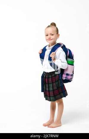 Nettes Mädchen in einer Schuluniform mit einem großen und schweren Rucksack auf weißem Hintergrund Stockfoto