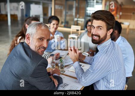 Wir alle tragen zum Planungsprozess bei. Porträt von zwei Geschäftsleuten, die mit ihren Kollegen im Sitzungssaal um einen Tisch sitzen. Stockfoto