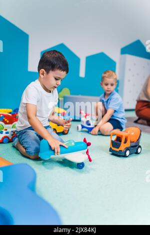 Spielzeit im Kindergarten. Kleinkinder Jungen sitzen auf dem Boden und spielen mit bunten Plastikautos, Booten, Flugzeugen und anderen Spielsachen. Hochwertige Fotos Stockfoto