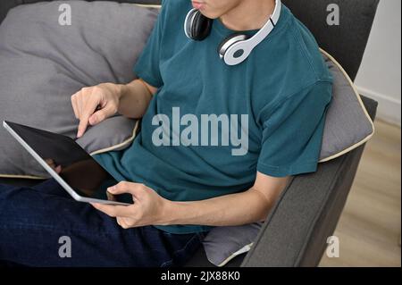Hipster junger asiatischer Mann mit digitalem Tablet-Touchpad, während er sich zu Hause entspannt. Zugeschnittenes Bild Stockfoto